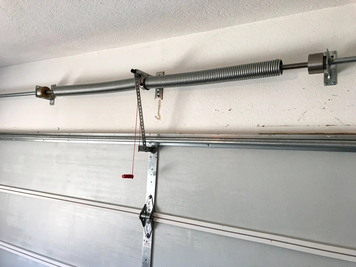 A garage door torsion spring is mounted above a white garage door.